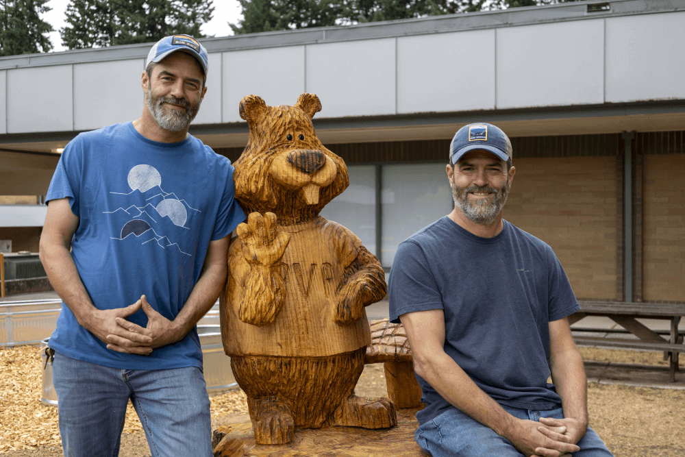 Patrick Bryson (left) and his twin brother Mike pose with the new Buddy the Beaver statue they helped carve